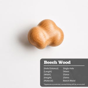 Peut inclure: Un bouton de meuble en forme de nuage en bois de h&ecirc;tre brun clair avec une surface lisse et arrondie. Le texte indique qu'il est en bois de h&ecirc;tre, poss&egrave;de un trou unique et mesure 54 mm de longueur, 35 mm de largeur et 29 mm de hauteur.