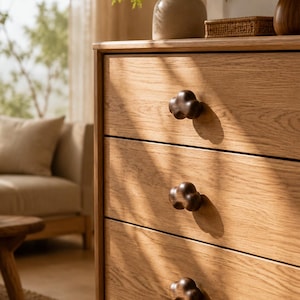 Puede incluir: Una cómoda de madera de color marrón claro con tres cajones horizontales. Cada cajón cuenta con un pomo de madera de color marrón oscuro con forma de nube. La veta de la madera es visible en los paneles frontales y tiene un acabado mate.