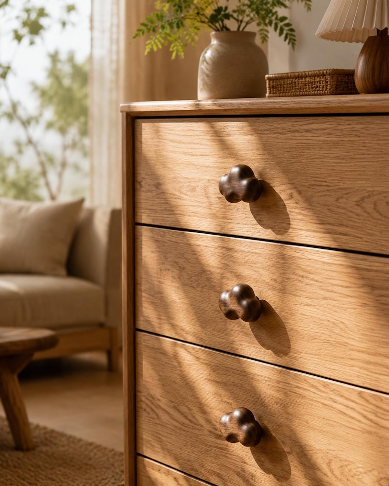 Peut inclure: Une commode en bois brun clair dot&eacute;e de trois tiroirs horizontaux. Chaque tiroir est &eacute;quip&eacute; d'un bouton en bois brun fonc&eacute; en forme de nuage. Le grain du bois est visible sur les fa&ccedil;ades et la surface pr&eacute;sente une finition mate et lisse.