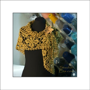 May include: A handmade, olive green crochet shawl with a floral design and a matching flower pin. The shawl is draped over a black mannequin, showcasing its intricate openwork pattern. The Studio-Era.com logo is visible in the bottom right corner.
