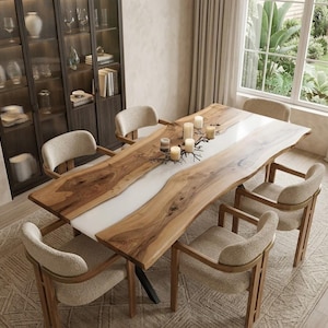 Pode incluir: Uma mesa de jantar retangular com um tampo de madeira natural de borda viva e uma incrustação central de resina branca, acompanhada por seis poltronas estofadas em bege claro com estrutura de madeira e cinco velas cilíndricas.
