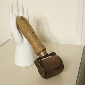 May include: A vintage roller with a wooden handle. The roller is made of metal and has a worn, rusty appearance.
