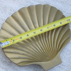 May include: A gold-colored brass seashell dish with a fluted design. The dish is approximately 11 inches wide.