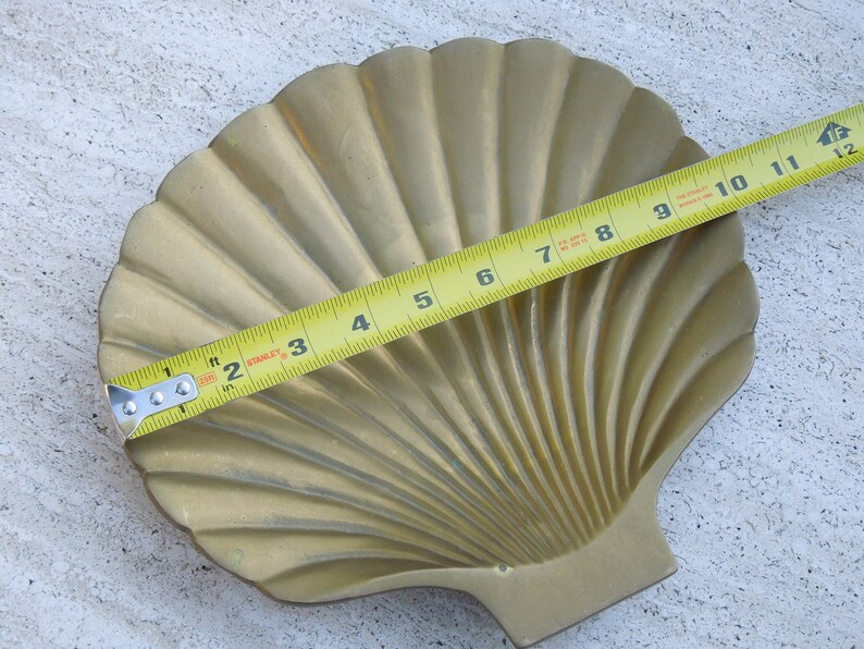 May include: A gold-colored brass seashell dish with a fluted design. The dish is approximately 11 inches wide.