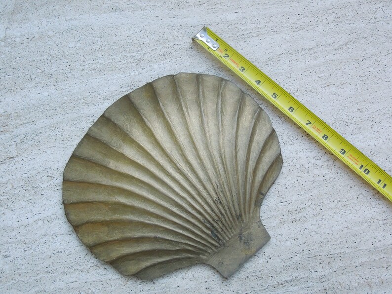 May include: A gold-colored metal seashell dish with a ribbed texture. The dish is approximately 6 inches wide.