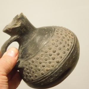 May include: A black ceramic jug with a handle and a textured design. The jug has a round body and a narrow neck.