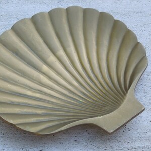 May include: A gold-colored metal seashell-shaped dish. The dish is made to look like a scallop shell with a ribbed texture.