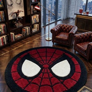Op de afbeelding: Een rond vloerkleed met een rood en zwart spinnenwebpatroon en twee grote witte, oogvormige accenten in het midden. Het kleed heeft een dikke, getextureerde pool en ligt op een donkere houten vloer in een kamer met boekenplanken en meubels.