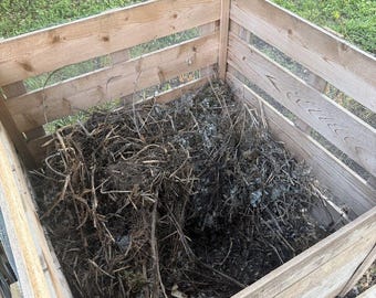 Pode incluir: Um recipiente de compostagem quadrado de madeira construído com ripas horizontais e painéis de rede metálica. O interior está cheio de uma pilha de ramos castanhos secos, detritos orgânicos de jardim e matéria vegetal em decomposição.