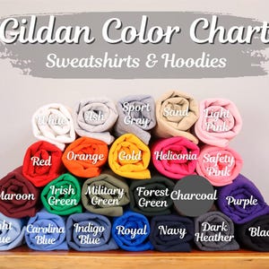 May include: A Gildan color chart for sweatshirts and hoodies displaying twenty-four rolled fabric samples in various colors including white, ash, sport gray, sand, light pink, red, orange, gold, heliconia, safety pink, maroon, irish green, military green, forest green, charcoal, purple, light blue, carolina blue, indigo blue, royal, navy, dark heather, and black.