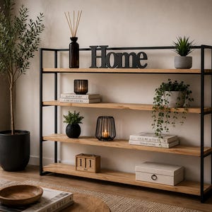 Peut inclure: Une étagère à quatre niveaux avec un cadre en métal noir et des étagères en bois clair. L'étagère supérieure présente un vase en verre foncé avec des roseaux, une enseigne en métal noir portant l'inscription Home et une petite plante en pot.