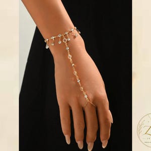 Pulsera de cadena para la mano en tono dorado con cristales y delicados dijes de cuentas