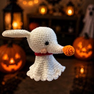 May include: A white crocheted ghost dog figure with a long snout, a small orange pom-pom nose, a black eye, and a red collar. The figure has a rounded head, one visible long ear, and a flared, skirt-like body made of white yarn stitches.