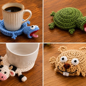 May include: A collection of four handmade crochet coasters shaped like animals, including a blue lizard, a green turtle, a black and white cow, and a tan beaver, each featuring detailed stitching, googly eyes, and distinct facial features.