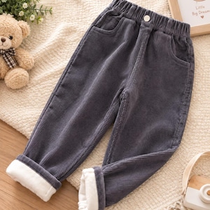 May include: Dark grey corduroy trousers featuring an elastic waistband with a single button closure, two front pockets, and a white fleece lining visible at the cuffed hems. The trousers have a textured ribbed fabric surface and a straight-leg cut.