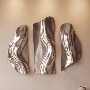 May include: A set of three wall-mounted decorative panels with a polished, reflective silver finish. Each panel features an irregular, organic shape with smooth, undulating curves that create a liquid-like appearance and distorted reflections.