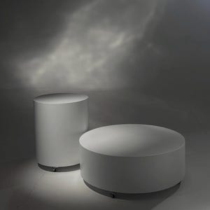 May include: Two white cylindrical pedestals of varying heights, both featuring smooth, solid surfaces and small, discreet casters at the base for mobility. The taller unit is narrow, while the shorter unit is wide and low, both in matte white.