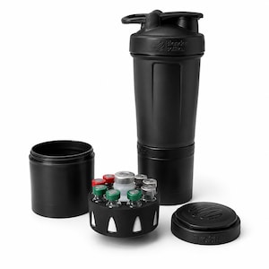 Puede incluir: Un vaso mezclador negro BlenderBottle ProStak con tapa, un recipiente de almacenamiento desmontable y una bandeja circular que contiene varios frascos de vidrio pequeños con tapas de colores. El logo BlenderBottle está grabado en la tapa.