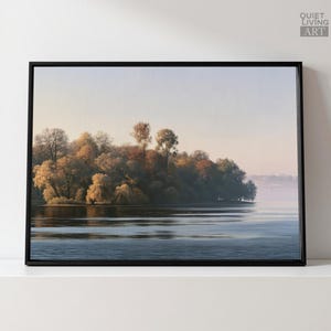 Könnte beinhalten: Ein gerahmter Landschaftsdruck mit einer dichten Baumgruppe mit herbstlich gefärbtem Laub entlang eines ruhigen Gewässers. Die Szene ist in weiches, dunstiges Licht getaucht, wobei sich die Bäume auf der Wasseroberfläche spiegeln. Der Text QUIET LIVING ART ist in der oberen rechten Ecke zu sehen.