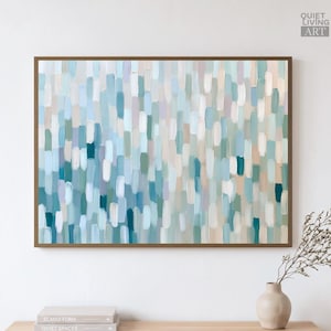 Könnte beinhalten: Ein rechteckiges Wandbild mit einem abstrakten Muster aus vertikalen Pinselstrichen in Hellblau, Türkis, Weiß und sanftem Beige. Das Gemälde ist in einen dünnen braunen Rahmen gefasst und zeigt in der Ecke den Text Quiet Living Art.