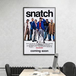 May include: A framed movie poster for Snatch featuring a group of six individuals standing in a line with a white dog on a leash in the center. The poster has a white background with the title Snatch in large black letters and coming soon below.