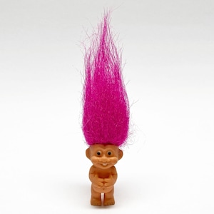 May include: A vintage troll doll with a smiling face and a tall, vibrant pink hair. The doll is made of a light brown plastic material and has its hands clasped in front. A nostalgic toy.