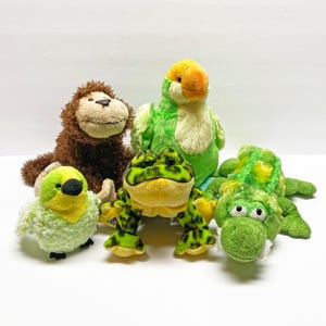 May include: A selection of soft toy animals, featuring a brown monkey, a green and yellow parrot, a green frog with black spots, a green alligator, and a small green bird. These colourful toys are suitable for children.