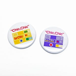 May include: Two white round buttons with the text "Chic, Chic" in red. One button has a yellow and green design with the text "Le Clic". The other button has a purple and yellow design with the text "Le Clic".