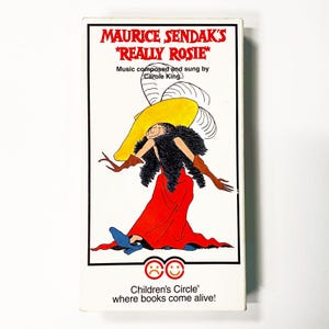 May include: A white rectangular box featuring the title "MAURICE SENDAK'S *REALLY ROSIE*". The illustration depicts a cartoon character in a red dress, yellow hat, and black fur. The text "Music composed and sung by Carole King" is also present.