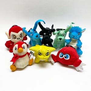 May include: A collection of plush toys in various colors and designs. The toys include a red monkey, blue elephant, black bull, green dog, blue creature, yellow creature, red crab, and a penguin. Each toy has a unique expression and design.