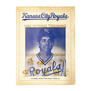 May include: A vintage 1982 Kansas City Royals Spring Training souvenir program featuring a blue-toned portrait of a baseball player wearing a cap with the KC logo. The cover includes team logos, game dates, and the text All Games 1:30 PM at Terry Park.