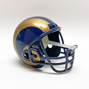 Könnte beinhalten: Miniatur-Footballhelm in Gold und Marineblau. Der Helm hat einen goldenen Streifen in der Mitte und eine marineblaue Gesichtsmaske. Ein Sammlerstück, ca. 15 cm lang.