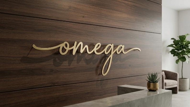 May include: A gold-colored metal sign featuring the word omega in a cursive script font. The lettering is mounted on a dark brown horizontal wood-paneled wall, creating a dimensional effect with a visible shadow cast behind the letters.
