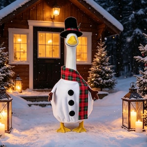 May include: A white goose figurine dressed as a snowman, wearing a black top hat with a red and green plaid band, and a matching red and green plaid scarf. The goose has three black circular buttons on its chest, brown wing-like arms, and yellow feet.