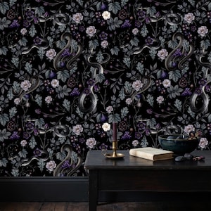 May include: Wallpaper featuring a repeating pattern of black snakes, purple grapes, figs, pinecones, and light purple flowers on a black background. A dark wooden table holds a brass candle holder with a purple candle and a bowl of fruit.