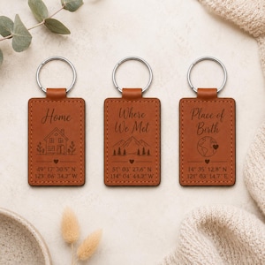 May include: Three rectangular tan leather keychains with silver metal rings. The first features a house icon and text Home 49 17 30.5 N 123 06 34.2 W. The second shows mountains and text Where We Met 51 03 27.6 N 114 04 44.2 W. The third shows a globe and text Place of Birth 14 35 12.8 N 121 03 14.7 E.