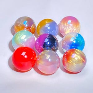 May include: A collection of nine spherical beads arranged in a three-by-three grid. Each bead features a smooth, glossy finish with iridescent, pearlescent, or solid vibrant colors including red, orange, yellow, blue, purple, and white.