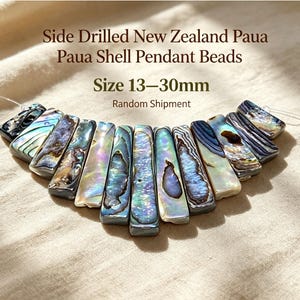 May include: Side drilled New Zealand Paua shell pendant beads in a range of iridescent colors including blue, green, and purple. The rectangular pieces are strung together, with text stating Side Drilled New Zealand Paua Shell Pendant Beads Size 13-30mm.