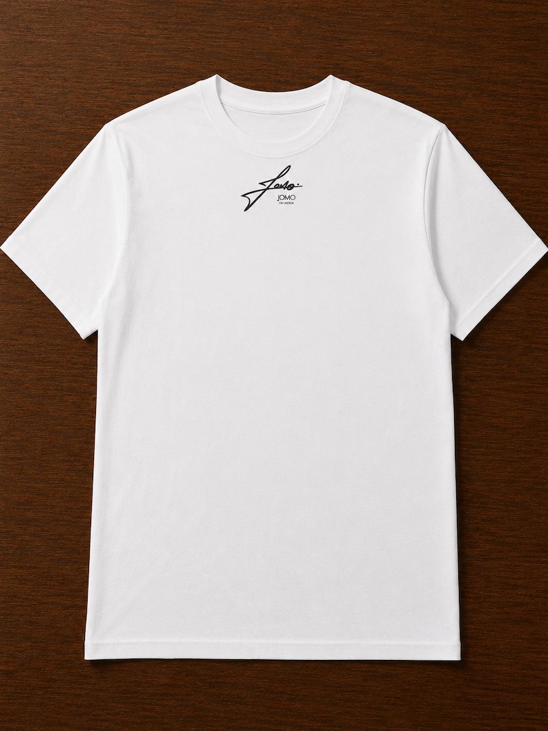 Pode incluir: Uma t-shirt branca de manga curta com um pequeno log&oacute;tipo gr&aacute;fico preto centrado na parte superior do peito. O log&oacute;tipo consiste numa escrita cursiva estilizada sobre o texto JOMO numa fonte sem serifa limpa e simples.