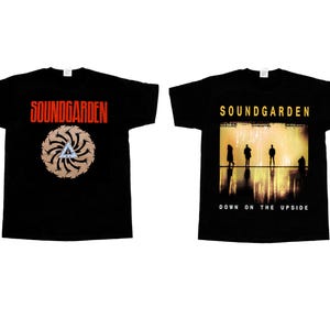 May include: A black short-sleeve t-shirt featuring a front graphic with the red text SOUNDGARDEN above a circular tan pattern and a blue triangle. The back graphic displays the yellow text SOUNDGARDEN above a scene of four silhouettes.