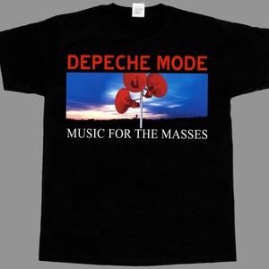 Può includere: Una t-shirt nera a maniche corte con una stampa grafica che riporta il testo DEPECHE MODE in rosso e MUSIC FOR THE MASSES in bianco. L'immagine centrale mostra tre altoparlanti rossi su un palo contro un cielo blu al tramonto.