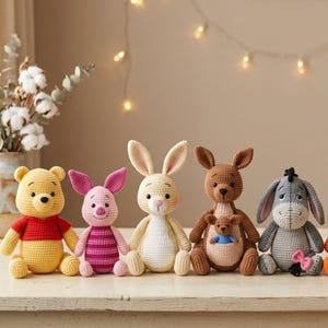 May include: A set of five crocheted stuffed animals including a yellow bear in a red shirt, a pink pig, a light tan rabbit, a brown kangaroo with a small joey in its pouch, and a gray donkey with a pink bow, all arranged in a row.