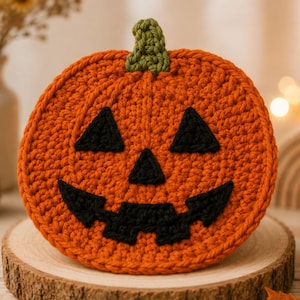 Peut inclure: Un dessous de verre rond en crochet orange repr&eacute;sentant une citrouille avec un visage de jack-o'-lantern, deux yeux triangulaires noirs, un petit nez triangulaire noir et une large bouche noire dentel&eacute;e. Une petite tige verte textur&eacute;e est au sommet.