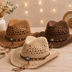 May include: Three crocheted straw hats in light beige, tan, and dark brown. Each hat features a wide brim, a pinched crown, and a decorative band with a central turquoise-coloured stone, wooden beads, and dangling braided cords with bead accents.