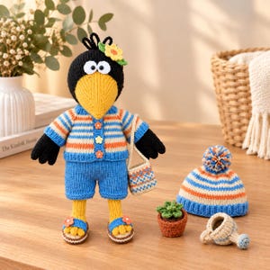 May include: A crocheted bird doll with a black head, yellow beak, and a small yellow flower accessory. It wears a blue, white, and orange striped cardigan with three flower buttons, blue shorts, and sandals. It carries a small striped bag.