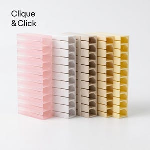 Pode incluir: Um conjunto de cinco organizadores de cabos verticais em rosa pastel, branco, bege e amarelo. Cada unidade retangular de plástico apresenta uma série de ranhuras horizontais para organização de fios. O texto Clique & Click está impresso em preto.
