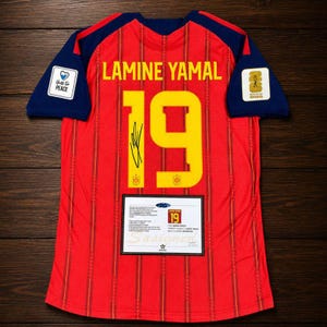 Puede incluir: Una camiseta de fútbol roja con mangas azul oscuro, con el nombre LAMINE YAMAL y el número 19 en amarillo. La camiseta incluye una firma negra sobre el número, un parche blanco 'Unites For PEACE', un parche de la Copa Mundial 2026 y un certificado.