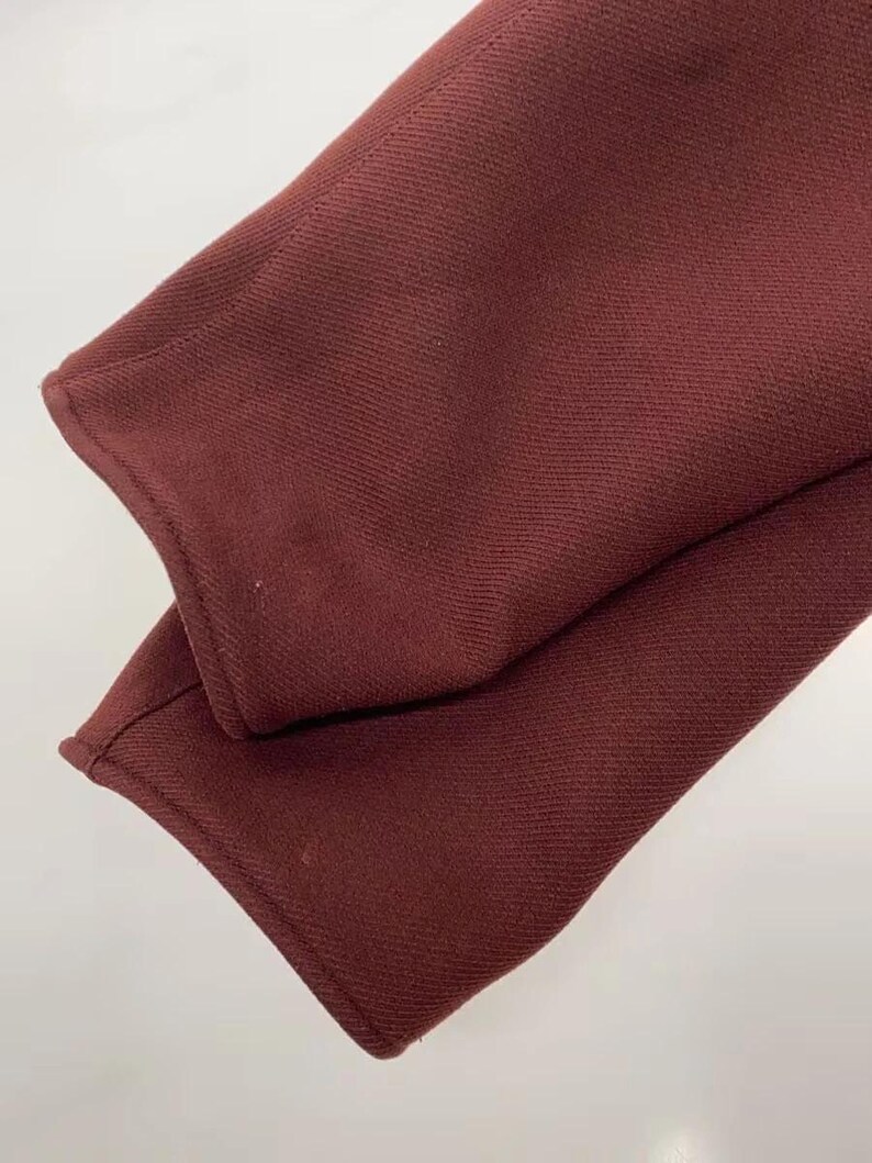 May include: A close-up view of the sleeves of a dark burgundy garment. The fabric features a distinct, fine diagonal twill weave texture. The cuffs are finished with clean, straight stitching along the edges, showing the deep red color.