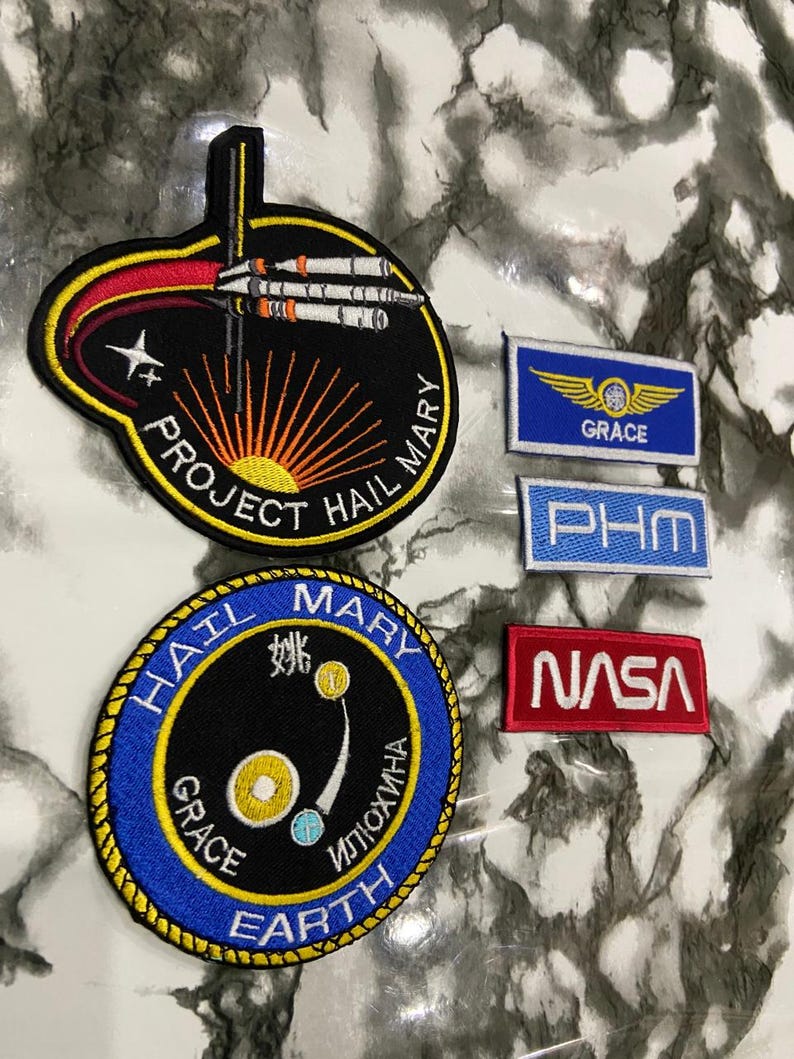 May include: A collection of five embroidered patches featuring space-themed designs. Two are circular, one with a black background and Project Hail Mary text, the other blue with Earth and Grace text. Three are rectangular with Grace, PHM, and NASA text.
