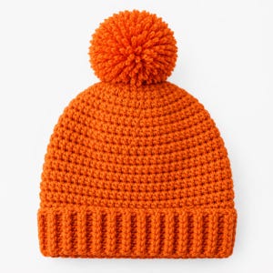 May include: A bright orange crochet beanie featuring a thick, ribbed brim and a large, matching yarn pom-pom attached to the top. The hat is constructed with a consistent, dense stitch pattern throughout the main body and a vertical ribbed texture.
